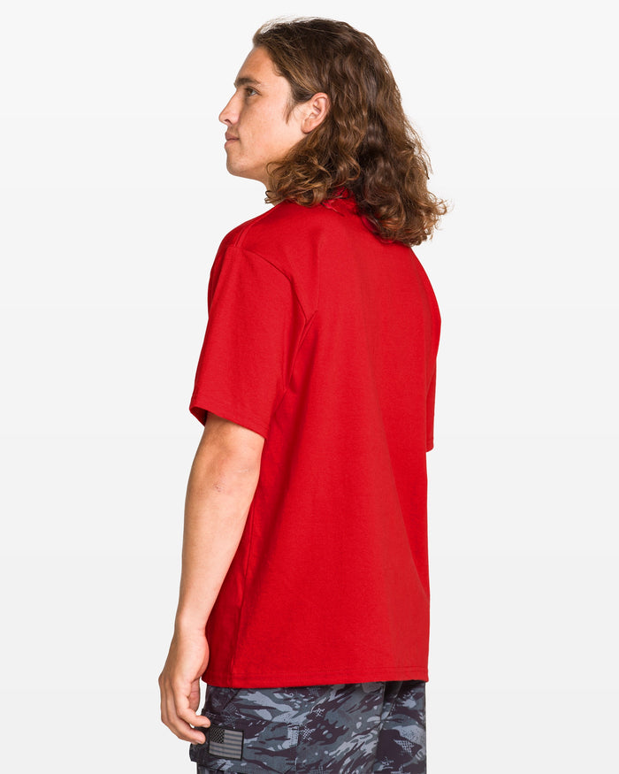A child with long wavy hair wears the Volcom Kids' Glory Daze Short Sleeve Tee in red and patterned black shorts, standing sideways against a white background.