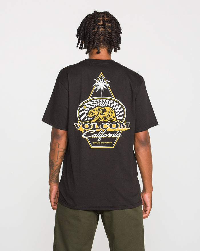 A person is seen from behind wearing the Volcom Men's Golden Bear Short Sleeve Tee, a black heavyweight cotton T-shirt. The back showcases a graphic with a bear, palm tree, checkered pattern, and the text "Volcom California, True to This," finished with the iconic Volcom Stone logo.