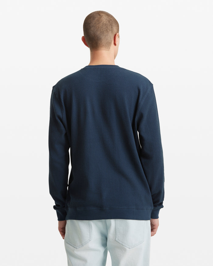 A person with short hair faces away, wearing the Volcom Men's Gridstone Crew Long Sleeve in dark blue with light-wash jeans, standing against a plain white background.