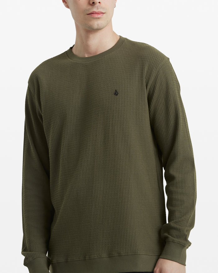 A man stands against a white background wearing the Volcom Men's Gridstone Crew Long Sleeve in olive green, featuring a waffle-knit texture, long sleeves, and a small black embroidered logo on the left chest.