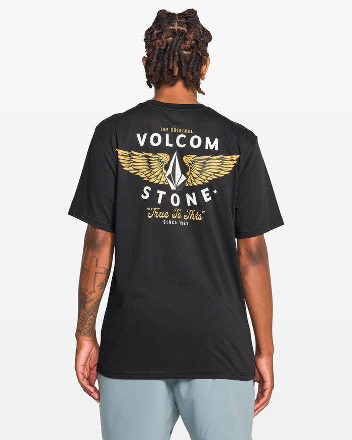 Seen from behind, a person with short dreadlocks wears the Men's Hi Flyer Short Sleeve Tee by Volcom—a black, soft ring spun cotton shirt with a large winged Volcom logo and “Volcom Stone, True To This, Since 1991” in white and yellow.