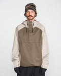 A man with a mustache wears the Volcom Men’s Hossegor 20K Pullover—a two-tone hooded jacket made from recycled V-Science shell with PFAS-free DWR—paired with black gloves and a camouflage beanie, standing against a plain white background.