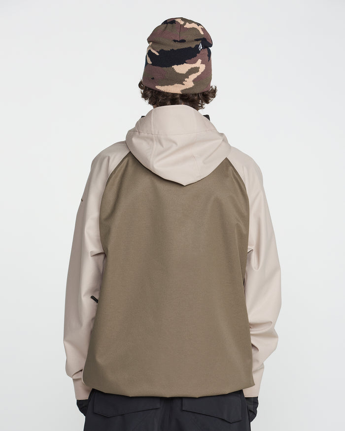 A person is standing with their back to the camera, wearing the Volcom Men’s Hossegor 20K Pullover in brown and beige, which features a recycled V-Science shell, along with a camouflage beanie. The background is plain white.