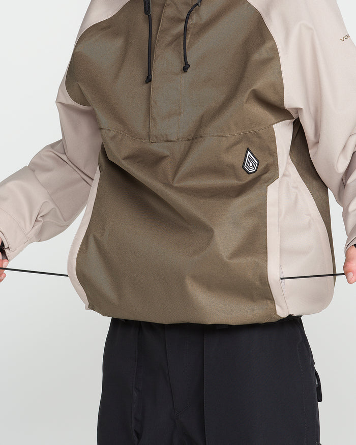A person adjusts the drawstrings on the hem of a brown and beige Volcom Men’s Hossegor 20K Pullover jacket while wearing black pants, with emphasis on the front and lower half of the jacket.