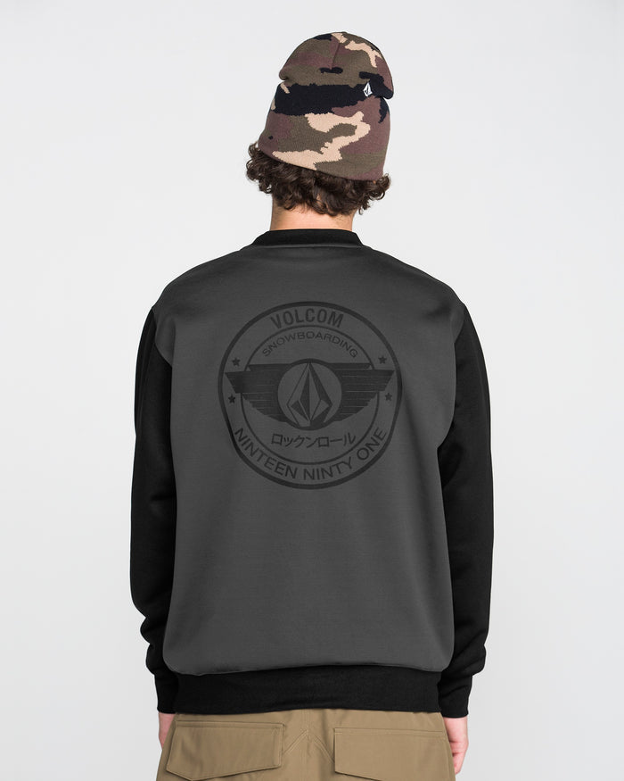 A person wearing a camo beanie and the Volcom Men’s Hydro Crew stands facing away, displaying a large Volcom logo and text on the back. Made from hydrophobic fleece for enhanced comfort, this crew features moisture-wicking properties to keep you dry. The background is plain and light-colored.