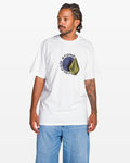 A man with braided hair and tattoos on his left arm wears the Volcom Men's Hypnotizer Short Sleeve Tee in white, featuring a circular black and yellow graphic and classic fit, paired with light blue jeans against a plain white background.
