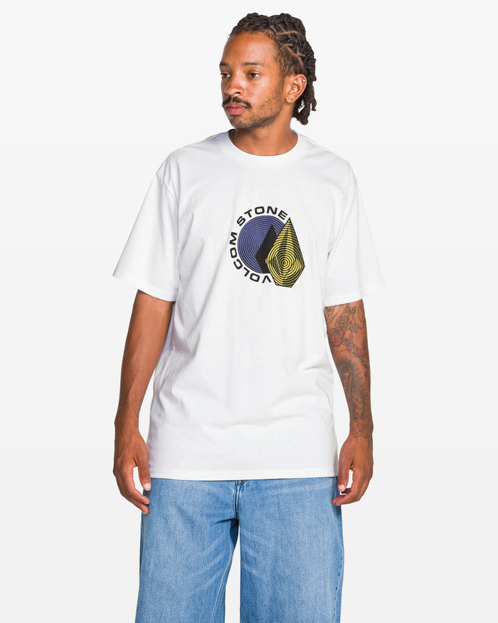 A man with braided hair and tattoos on his left arm wears the Volcom Men's Hypnotizer Short Sleeve Tee in white, featuring a circular black and yellow graphic and classic fit, paired with light blue jeans against a plain white background.