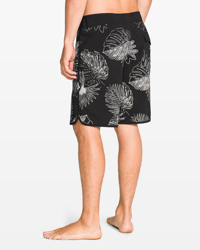 A person stands barefoot, facing away, wearing Volcom Men's Infuse Scallop Mod 19" boardshorts with a white tropical leaf pattern and Cinch Fly Technology. The background is plain white.