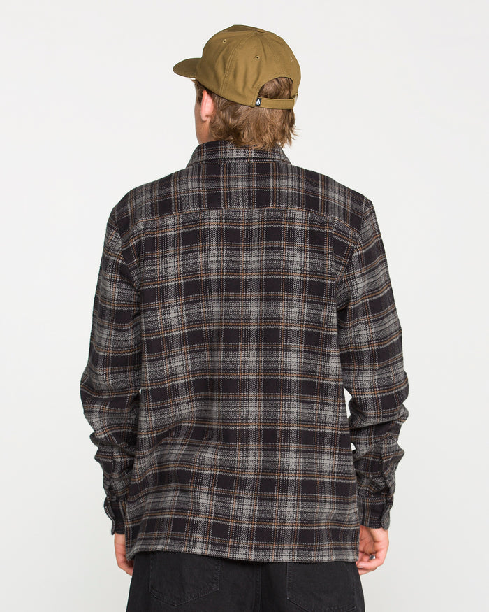 A person wearing a brown cap and a dark Volcom Men's Johnstone Long Sleeve Shirt is facing away from the camera against a plain white background.