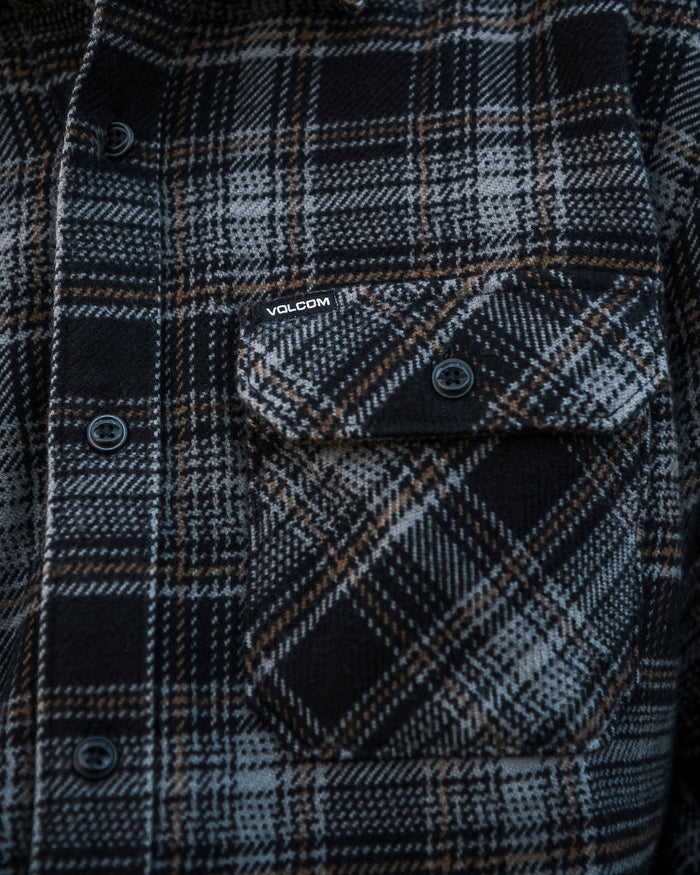 A close-up of the Volcom Men’s Johnstone Long Sleeve Shirt, a black, gray, and brown plaid heavyweight flannel featuring a buttoned chest pocket with a small Volcom woven label above it.