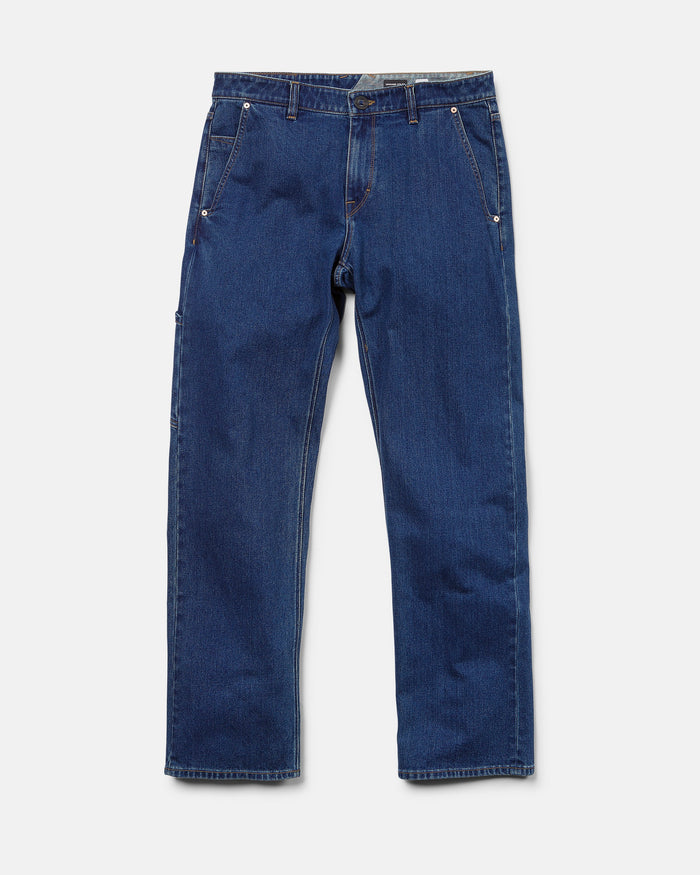 The Volcom Men's Kinkade Utility Denim Pants—a timeless pair of straight leg jeans in classic indigo, featuring front and back pockets, silver rivets, and a button closure—are laid flat on a white background.