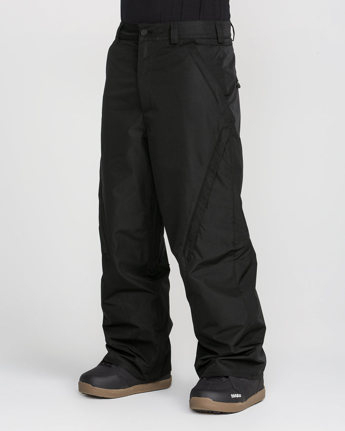 A person is wearing baggy black Volcom Men’s Kleveland Pants and black snow boots with brown soles, standing against a plain light background. Only the lower half of the body is visible in the image.