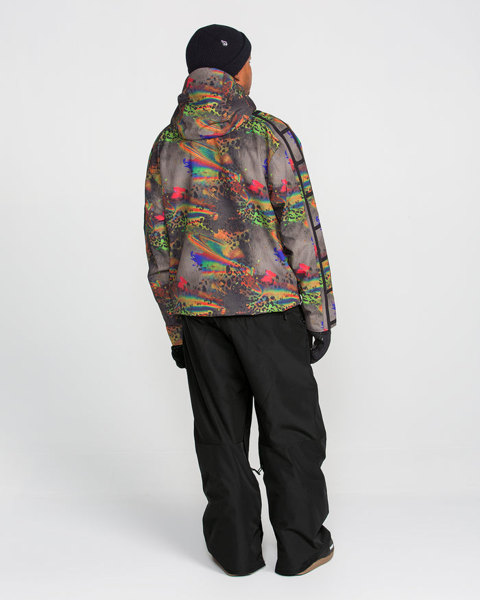 A person stands facing away against a plain white background, wearing baggy Volcom Men’s Kleveland Pants, a colorful patterned hooded jacket, black gloves, and a black beanie.