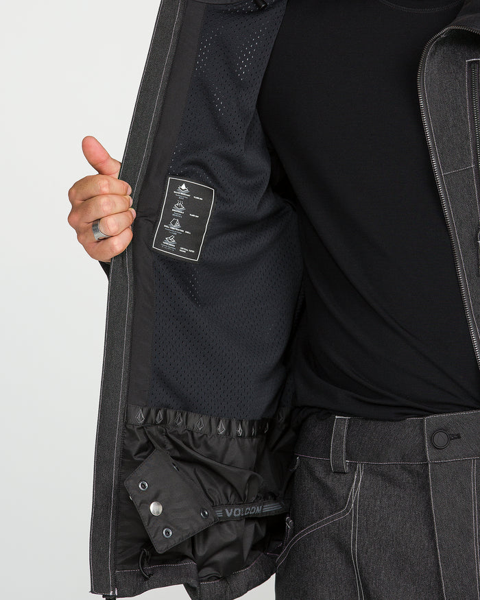 A person wearing a black shirt and gray jacket holds the jacket open to reveal its mesh interior lining, care-instruction tag, and a buttoned inner pocket—perfectly paired with Volcom Men’s Lapper Pants for a casual yet functional winter look.