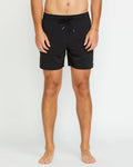 A barefoot model stands against a plain white background, wearing Volcom Men's Lido 2 Solid Trunks in black, made from recycled polyester. The image is cropped below the chest, with the face not visible.