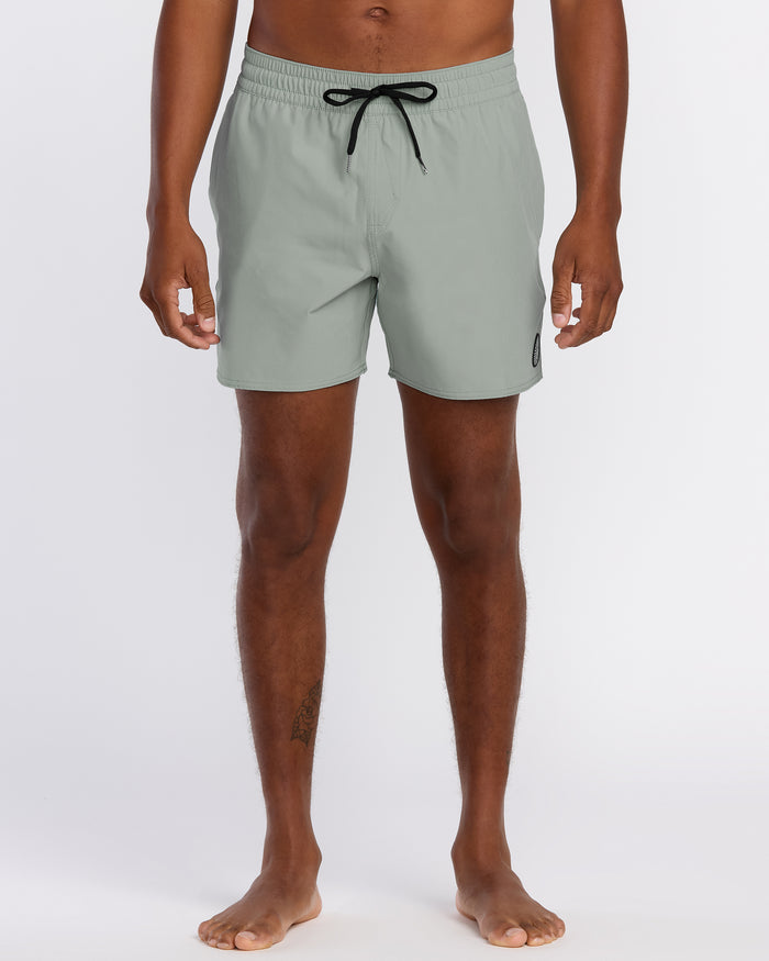 A person stands barefoot in Volcom Men's Lido Solid 16" Trunks, light gray with a black drawstring and small logo on the left leg. The 2-way stretch swim trunks are cropped at the torso; background is plain white.
