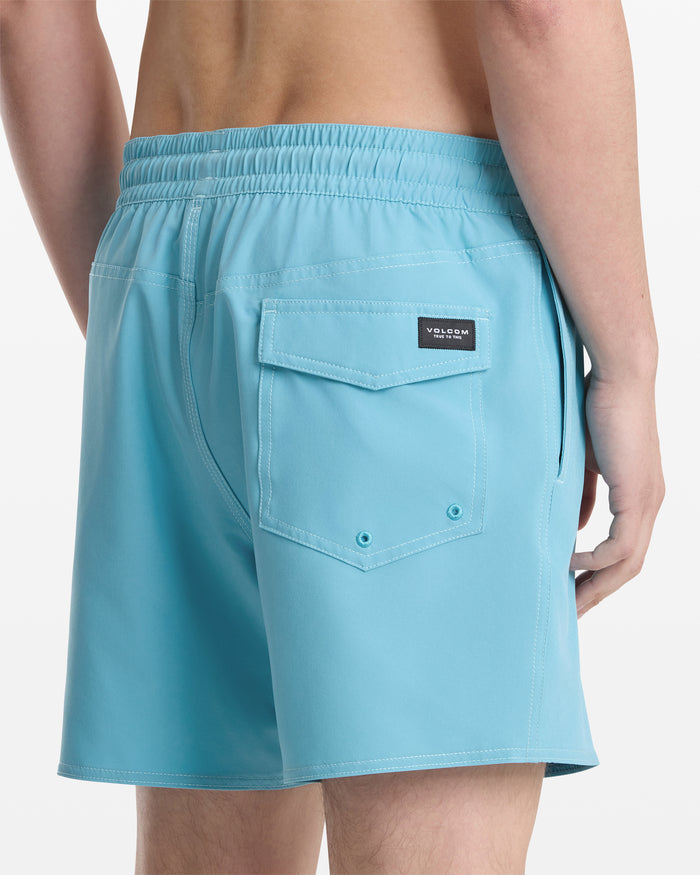 A person wearing Volcom Men's Lido Solid Trunk 16 in light blue, shown from the back waist down. The swim trunks feature an elastic waistband, a flap back pocket, and a small Volcom brand label.