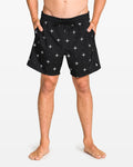 A person stands barefoot in Volcom Men's Lido Print 16" Trunk shorts with a white star print, elastic waistband with drawstring, 4-way stretch, and side pockets. The background is plain white.