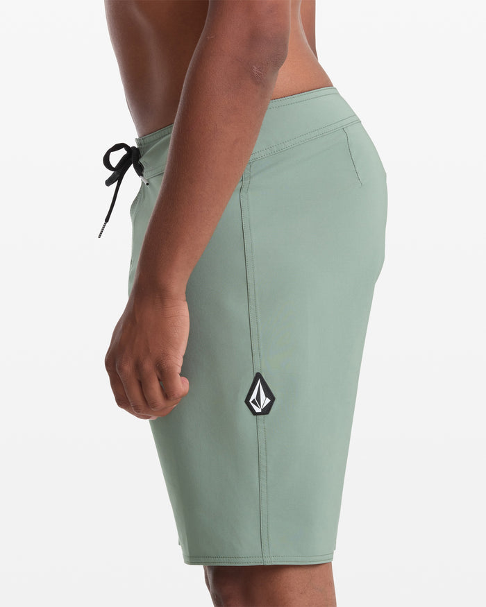 A person wears Volcom Men's Lido Solid 20" Trunks in light green with a black drawstring and black and white logo patch, standing against a plain white background.
