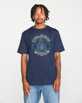 A person wearing a Volcom Men's Line Feld Short Sleeve Tee in navy blue heather, made from soft ring spun cotton, and light blue jeans stands against a plain white background, looking at the camera with a neutral expression.
