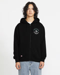A person with wavy dark hair models the Volcom Men's Lineage Zip Fleece, a relaxed fit black hoodie with a small green and white left chest graphic, paired with light blue jeans against a plain white background.