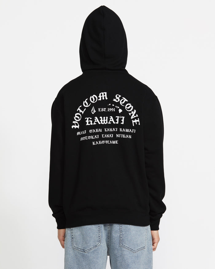 A man wears the Volcom Men's Lineage Zip Fleece, a black relaxed-fit hoodie with "Volcom Stone Hawaii" and smaller white text on the back. He stands facing away from the camera against a white background.
