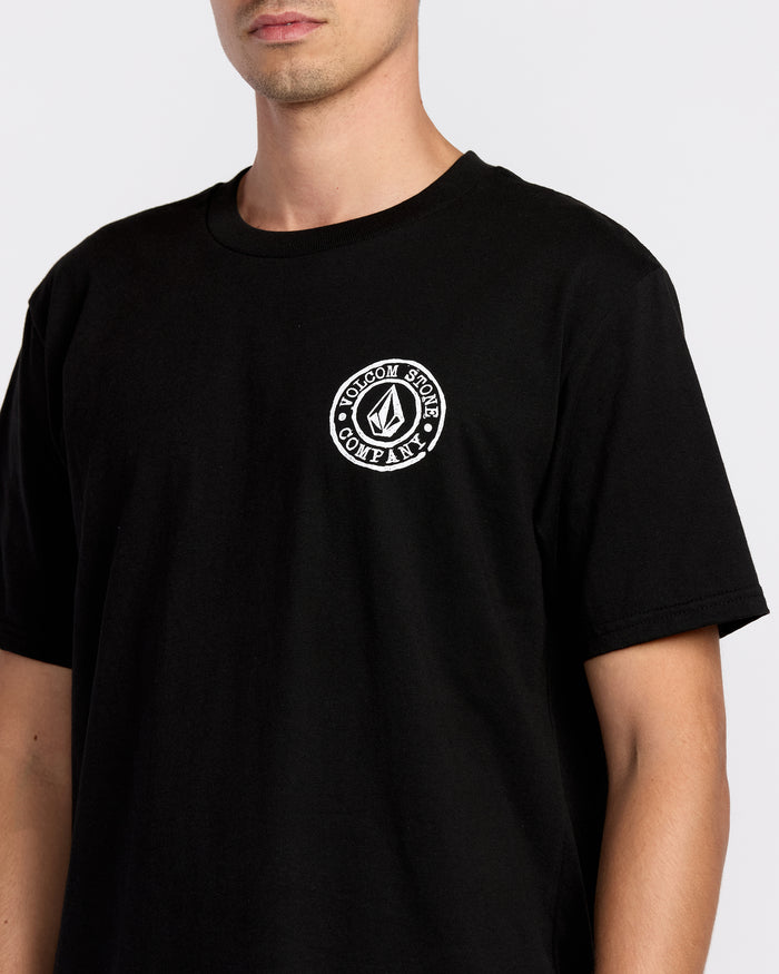 A person wears the Volcom Men’s Logo Stamp Short Sleeve Tee, a black heavyweight t-shirt featuring a small round Volcom Stone Company logo on the left chest. The photo captures the upper torso against a plain background.