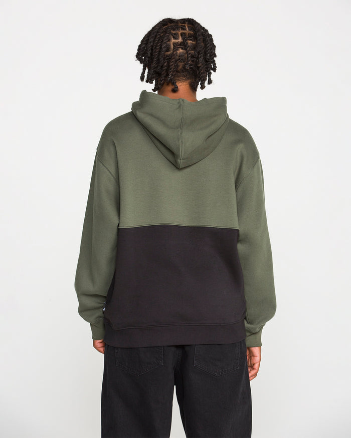 A person with braided hair is seen from behind against a plain white background, wearing the Volcom Men's Long Division Pullover. The hoodie showcases green and black colorblocked panels and is paired with black pants. Crafted with REPREVE recycled fibers, this eco-conscious pullover combines style and sustainability.
