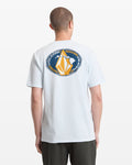 A person viewed from behind wears the Volcom Men's Loopy Short Sleeve Tee in light blue, featuring a circular graphic with "VOLCOM HAWAII" and a stylized yellow and white design on the back.