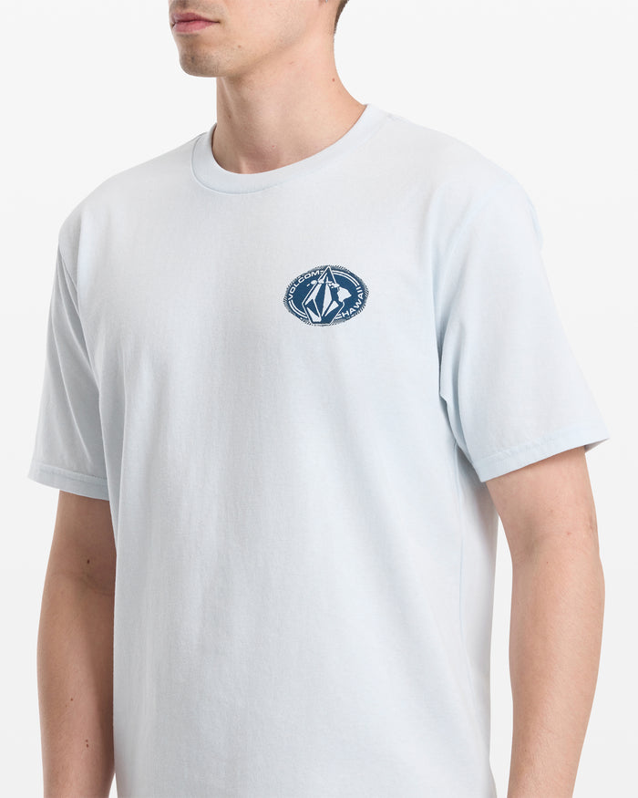 A person wears the Volcom Men's Loopy Short Sleeve Tee in light blue, featuring a small dark blue geometric logo and text on the left chest. The background is plain white, and their head is partially out of frame.
