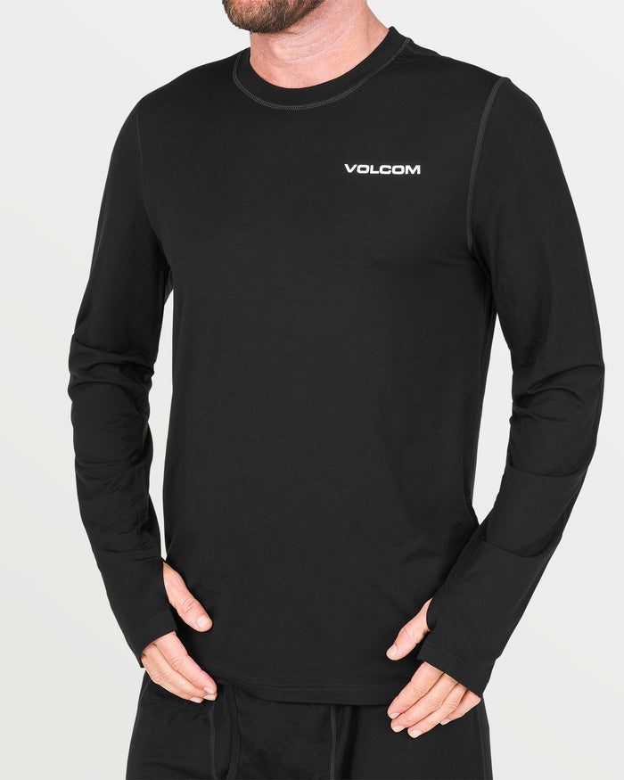 A person is wearing the Volcom Men’s M Merino Blend Crew, a black long-sleeve base layer featuring “VOLCOM” in white on the chest. Designed for men, this shirt includes thumbholes for enhanced comfort and practicality. The individual is standing against a plain light background.