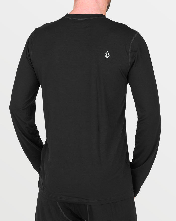 A person wearing a Volcom Men’s M Merino Blend Crew, a plain black long-sleeve base layer shirt featuring a small white logo on the upper back, stands with their back to the camera.