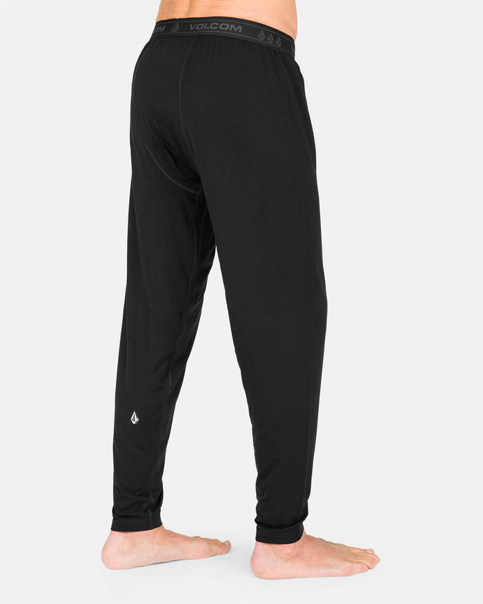 A person is shown from the back, standing barefoot on a white background and wearing Volcom Men’s M Merino Blend Pants. These men’s base layer pants are made with a merino blend for quick-dry performance and all-day comfort.