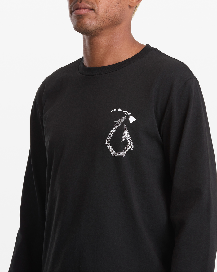 A person wearing the Volcom Men’s Makau Long Sleeve Tee, featuring a black design with a white stylized fish hook and small island shapes on the upper left chest.
