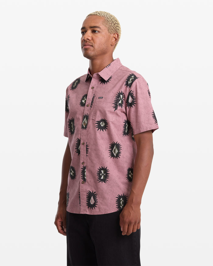 A man with short blond hair models the Volcom Men's Markerstone Short Sleeve shirt, which features an allover black and white abstract sunburst print, standing against a plain white background.