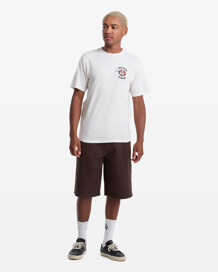 A person with short blond hair wears the Volcom Men's Mister Stone Short Sleeve Tee, dark brown knee-length shorts, white crew socks, and black sneakers, standing against a plain white background.