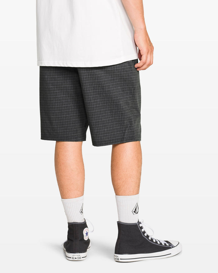 A person wearing a white T-shirt, Volcom Men's Mix Frickin Cross Shred Shorts, a recycled buckle button, white socks with a black logo, and black high-top Converse sneakers stands against a plain white background.
