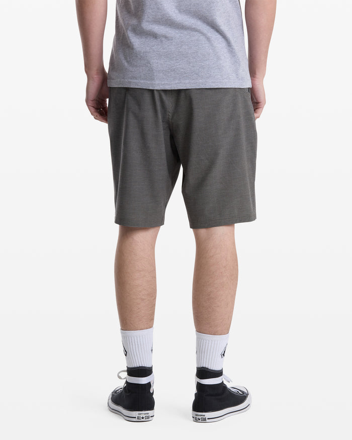 A person stands facing away in Volcom Men's Mix Frickin Cross Shred Shorts (dark gray), a gray T-shirt, white crew socks with a black logo, and black low-top sneakers against a white background.