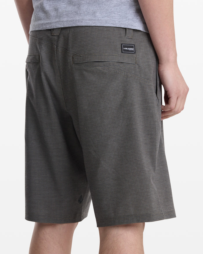 A person shown from the waist down and back wears gray plaid Volcom Men's Mix Frickin Cross Shred Shorts and a gray shirt, with their right hand resting by their side.