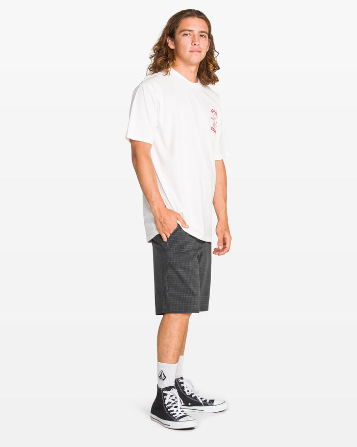 A person with long hair stands against a white background, wearing a white T-shirt, Volcom Men's Mix Frickin Cross Shred Shorts, white socks, and black high-top sneakers. One hand is in the pocket while the other hangs by their side.