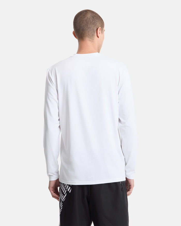 A person with short hair wears a Volcom Men's Modstone Loose Long Sleeve rashguard in white and black graphic shorts, standing with their back to a plain light background.