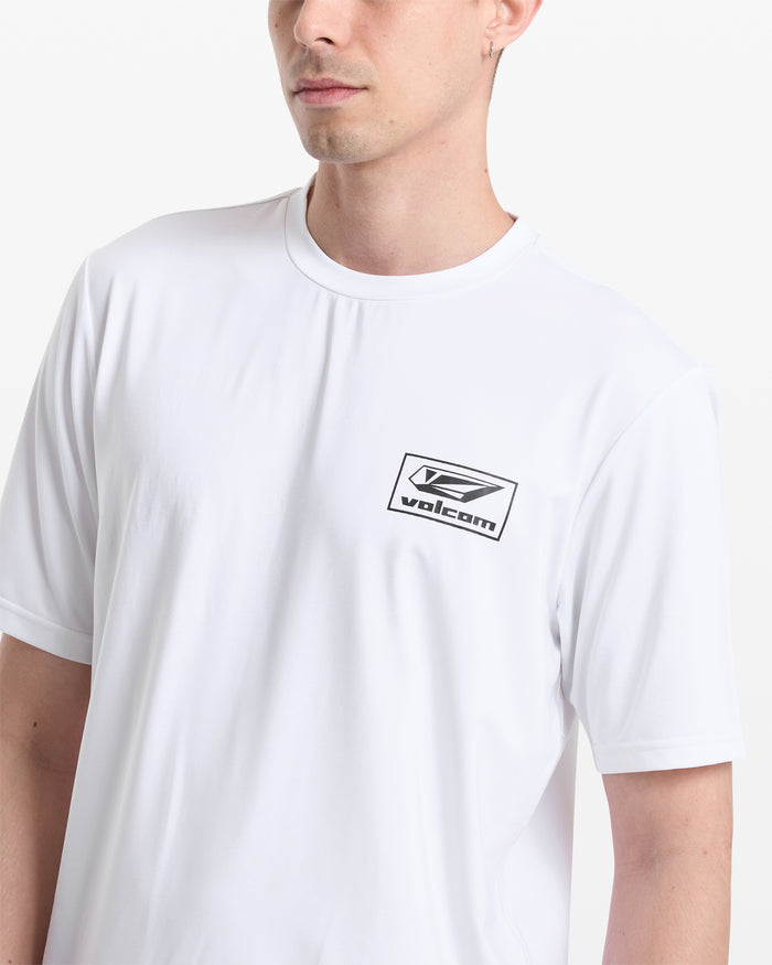 A man wears the Volcom Men's Modstone Loose Short Sleeve Surf Tee, a relaxed fit plain white t-shirt with a small black Volcom logo on the left chest, thrashguard style, standing against a white background.