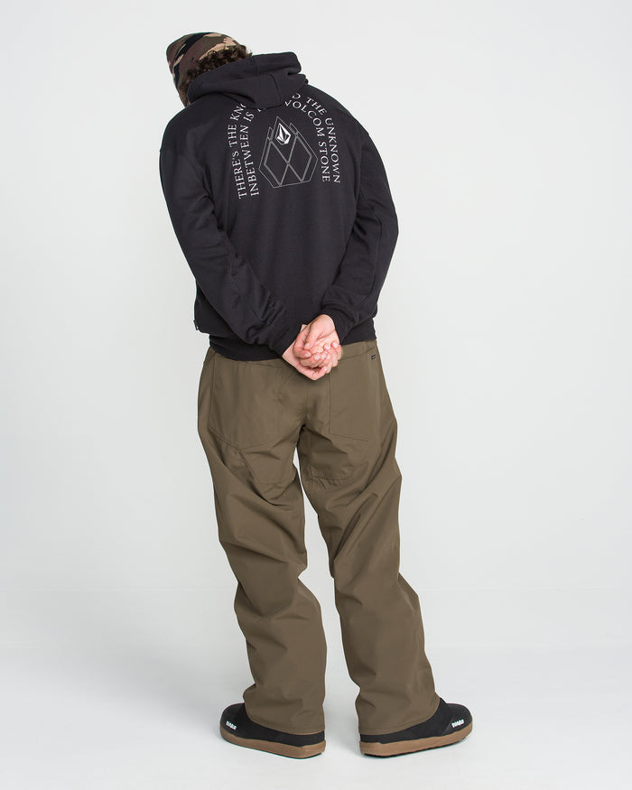 A person in a black hoodie with a white graphic and brown pants stands facing away, hands clasped behind their back, wearing a camo beanie and black shoes against a plain white background—the look is completed with Volcom Men’s Nailer Pants, designed for urban style and mountain-ready comfort.