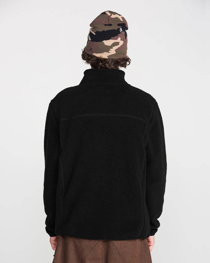 A person with curly hair wears the Volcom Men’s Nelson Sherpa Full Zip in black and a brown camo beanie. They are facing away from the camera against a plain white background.