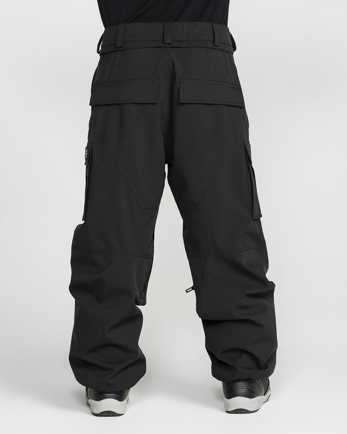 A man is seen from the back, standing against a plain white background, wearing Volcom Men’s Nwrk 20K Baggy Pants—loose-fitting black cargo pants made from recycled shell fabric, featuring multiple pockets and a baggy silhouette.