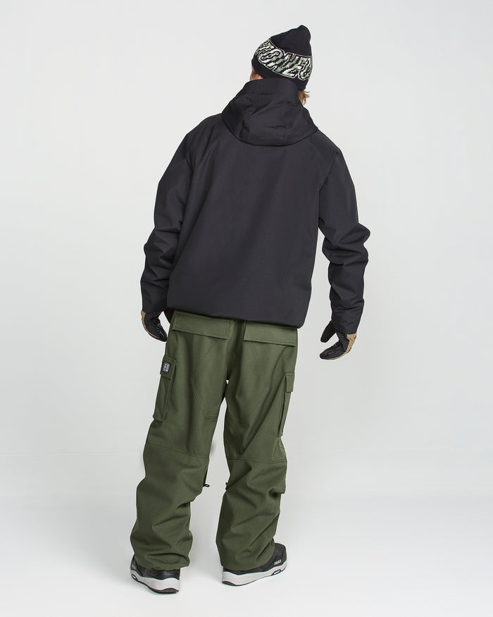 A person stands with their back to the camera against a plain white background, wearing a black jacket, Volcom Men’s Nwrk 20K Baggy Pants—styled like men’s snow pants with 20K waterproof protection—in olive green, paired with black winter boots, gloves, and a black patterned beanie.