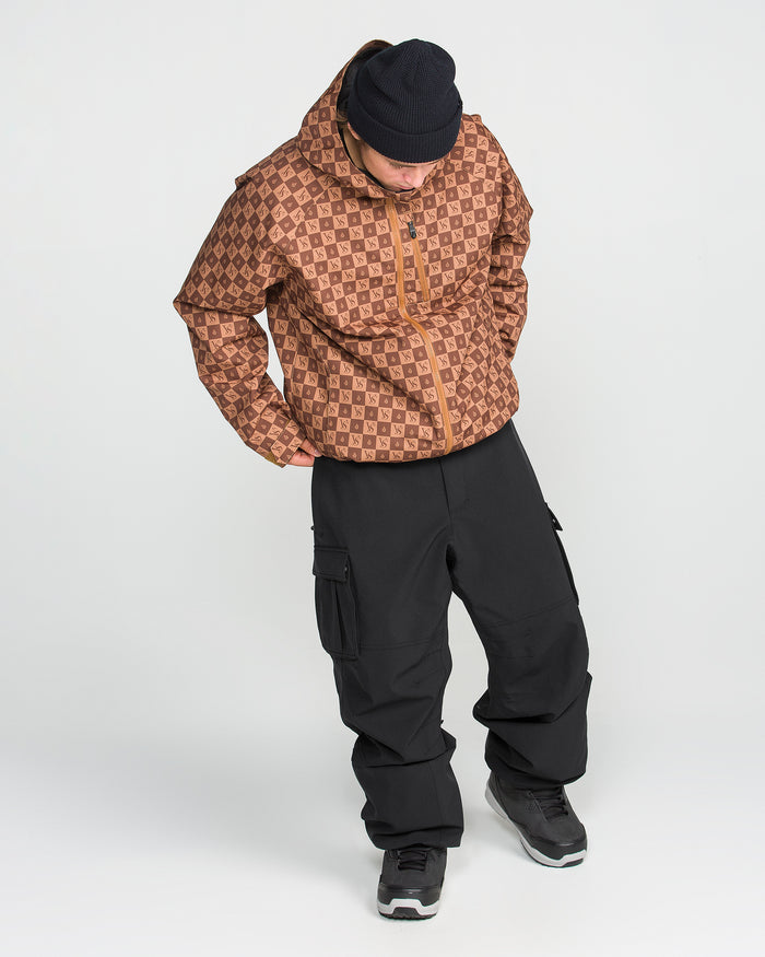 A person wearing a black beanie, a brown patterned jacket with a recycled shell, and Volcom Men’s Nwrk 20K Baggy Pants stands looking down with hands in pockets against a plain white background.