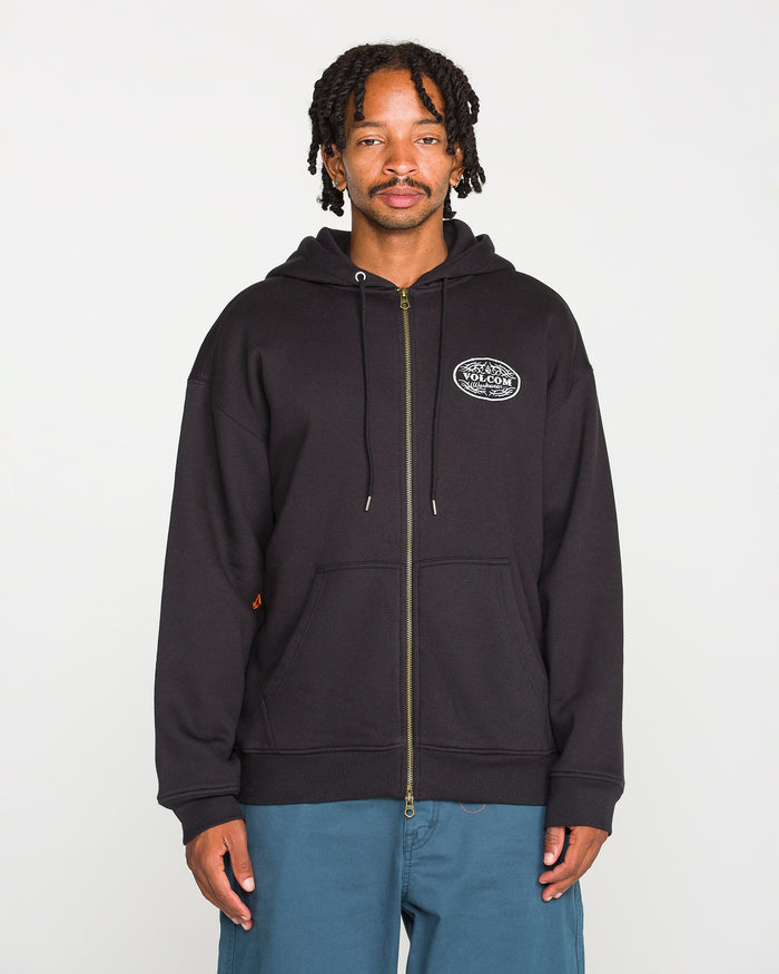 A man with short dreadlocks wears the Volcom Men’s On The Hunt Workwear Zip fleece hoodie with cotton waffle thermal lining and blue pants, standing against a plain white background and looking at the camera with a neutral expression.