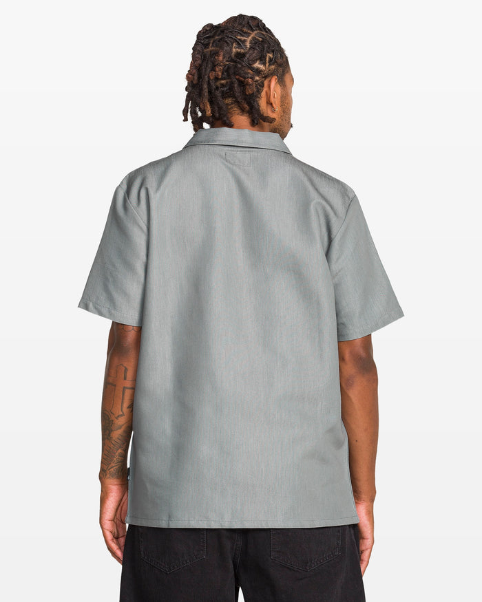 A person with short dreadlocks, seen from behind, wears the Volcom Men's Otis Stone Short Sleeve Tee and black pants against a plain white background.