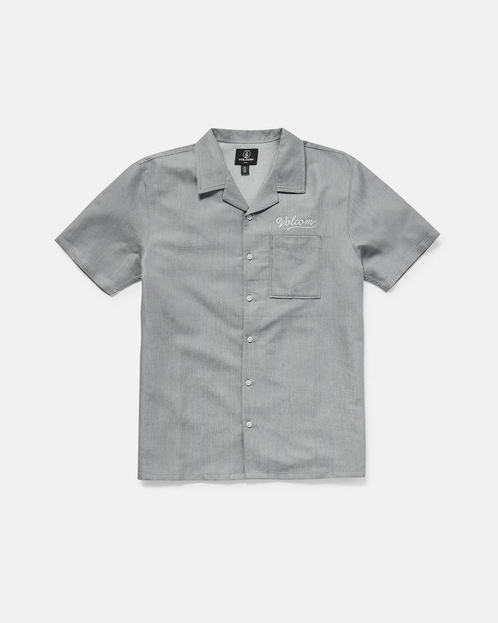 The Volcom Men's Otis Stone Short Sleeve Tee is a light gray, boxy-fit tee with a collar, made from textured fabric. It has a single chest pocket with "Welcome" embroidered above it in white.